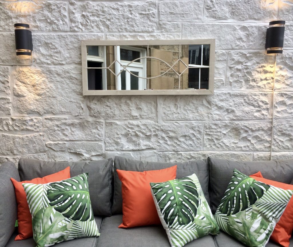 A contemporary outdoor mirror and tropical cushions add a designer touch to this Edinburgh garden.