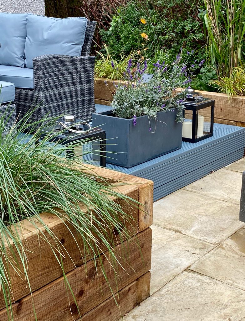 Modern design for decking with vibrant grasses and styled with lanterns, outdoor furniture and plant pots.