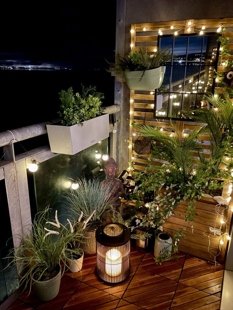 Balcony garden with artificial potted plants and city skyline in the background at night.