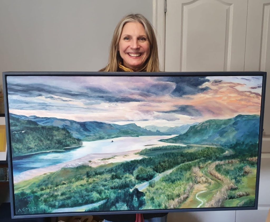 Angela Moffat, Edinburgh-based artist, holding a framed commissioned painting of a stunning Oregon national park landscape, showcasing her talent in custom art