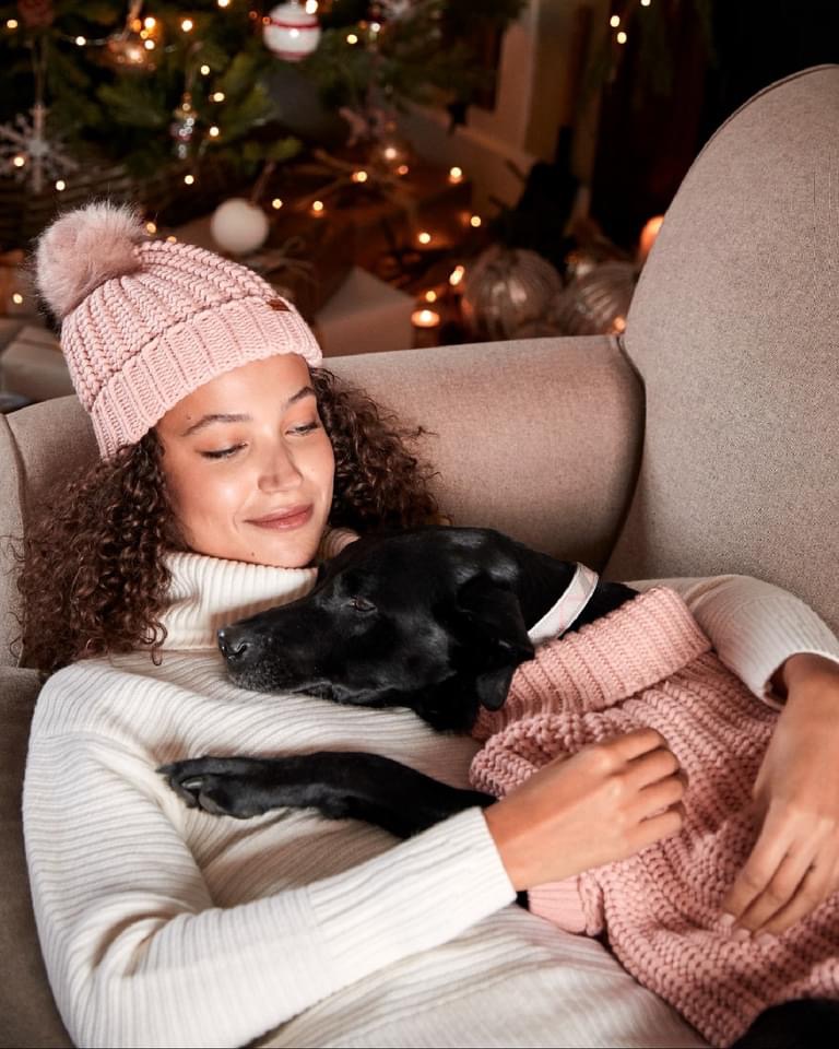 A cozy scene with a woman in a Barbour knit sweater snuggling with her dog dressed in matching pink knitwear, styled by Angela Moffat, Stylist, Edinburgh, Scotland