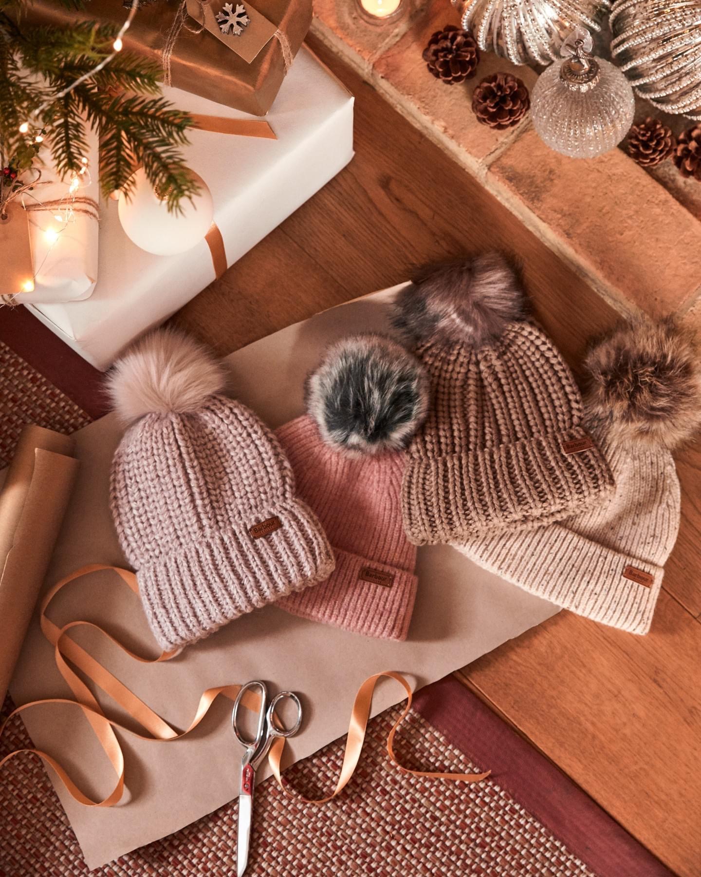 A flatlay of Barbour knitted hats with faux fur pom-poms, surrounded by Christmas decorations, styled by Angela Moffat, Stylist, Edinburgh, Scotland