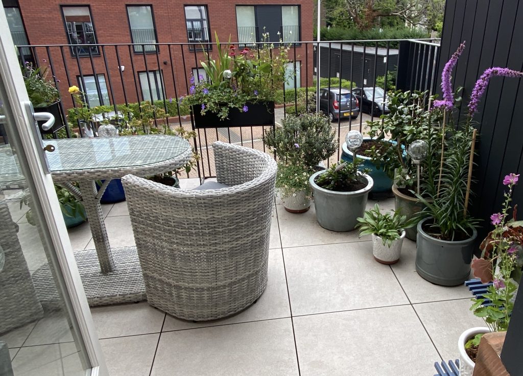 Stylish balcony with woven furniture and lush potted plants.