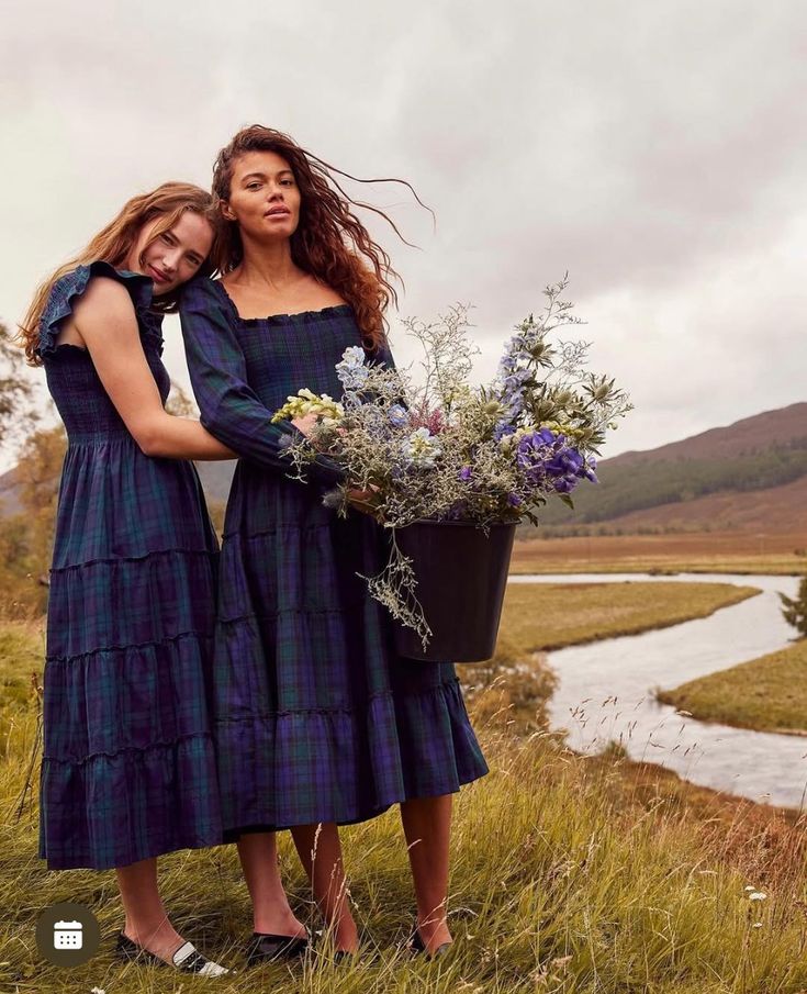 Two models in matching tartan dresses holding a bucket of wildflowers by a riverside in the Scottish Highlands. Styled by Angela Moffat, Stylist, Edinburgh, Scotland