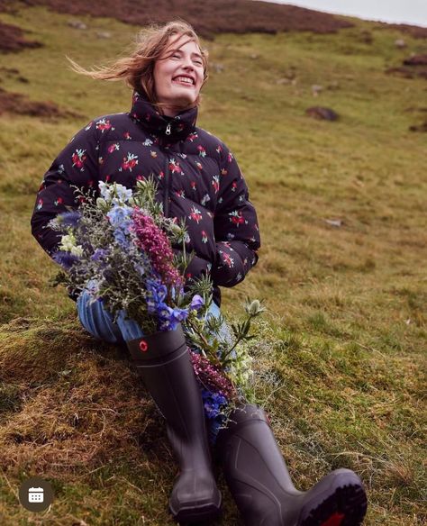 Smiling model seated in a Highland field holding a bouquet of wildflowers, wearing a floral coat. Styled by Angela Moffat, Stylist, Edinburgh, Scotland