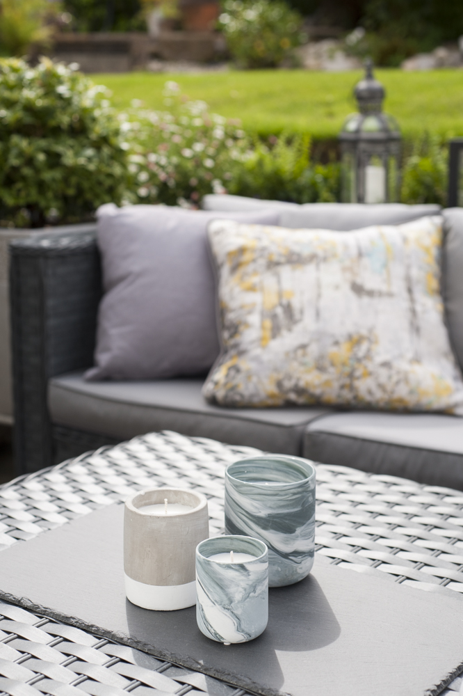 Outdoor coffee table with marbled candles and soft grey cushions in the background.